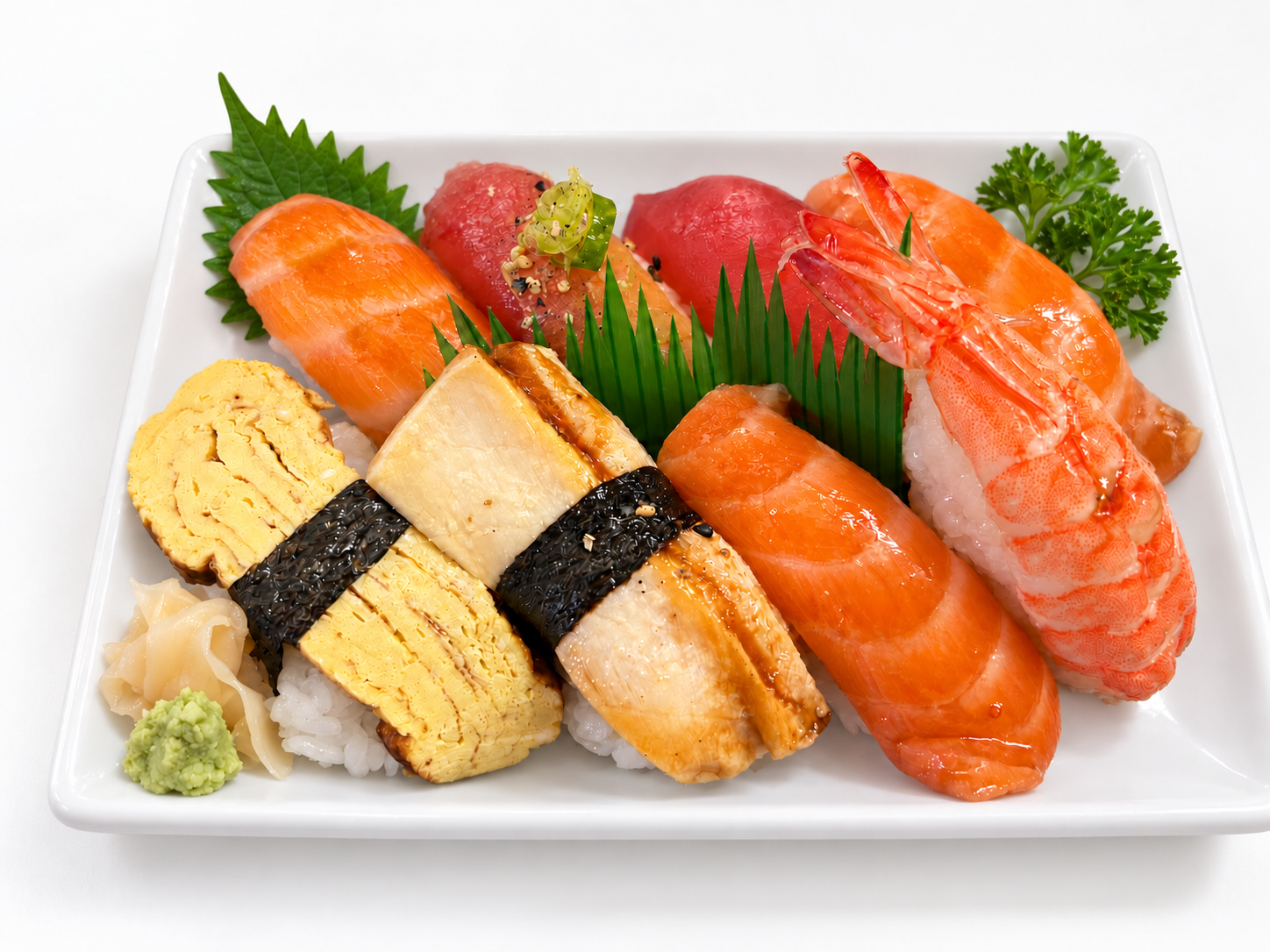 Assorted nigiri on a white plate with ginger and wasabi